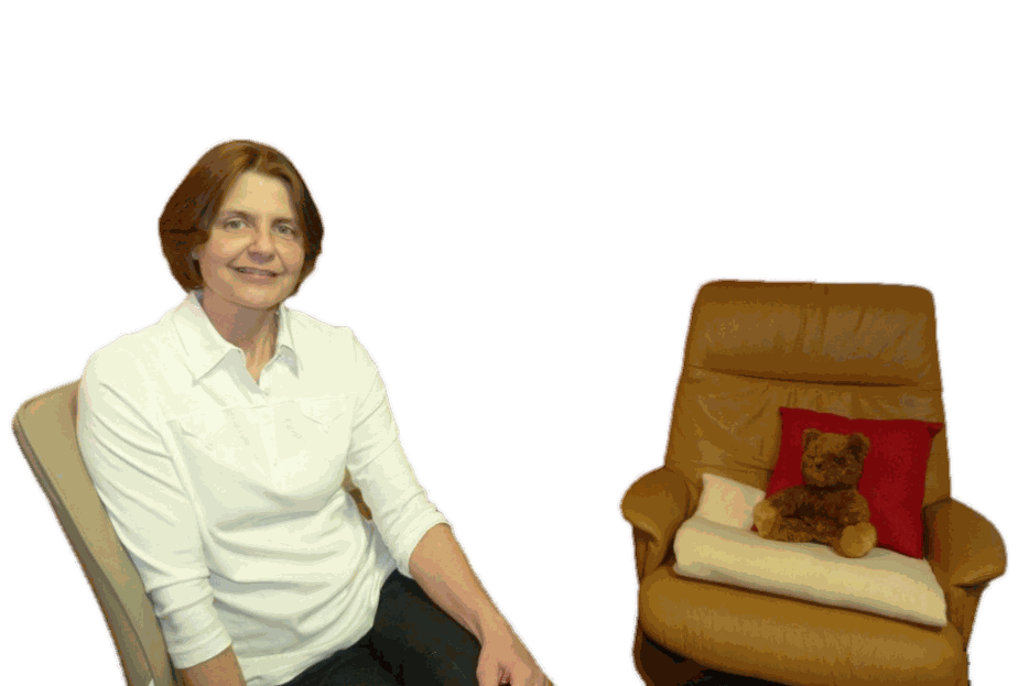 Birgit Rudolph-Schuster im Praxisraum, daneben ein Sessel mit Kissen und Teddybär